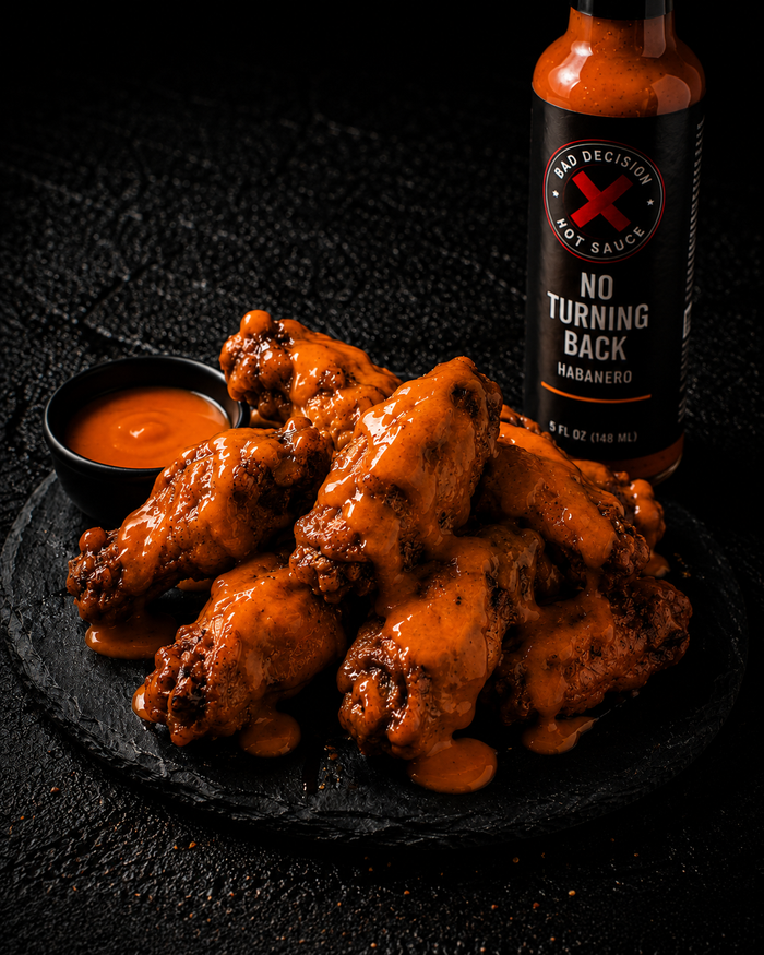 Chicken wings coated in orange habanero sauce on a dark slate plate, beside a bottle of No Turning Back habanero hot sauce