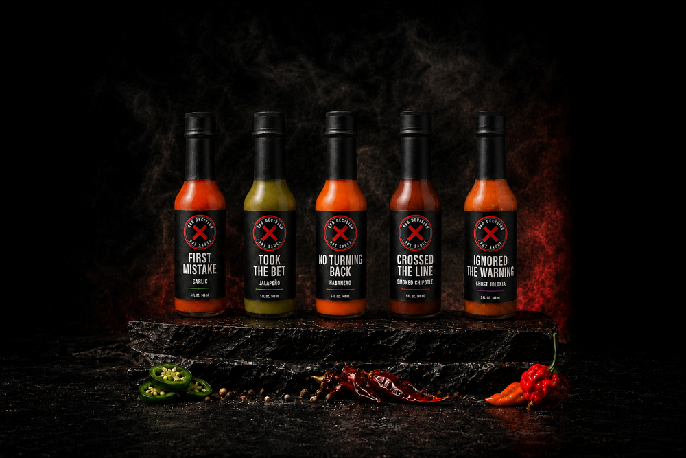 All five Bad Decision Hot Sauce bottles in heat order — First Mistake garlic, Took The Bet jalapeño, No Turning Back habanero, Crossed The Line smoked chipotle and Ignored The Warning ghost jolokia
