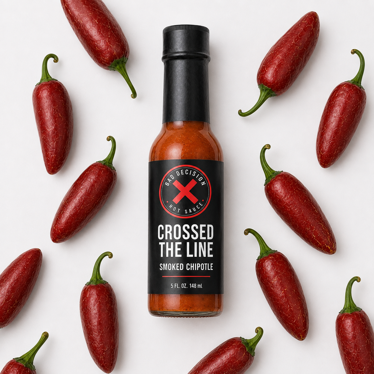 Crossed The Line smoked chipotle hot sauce bottle lying among dried chipotle peppers