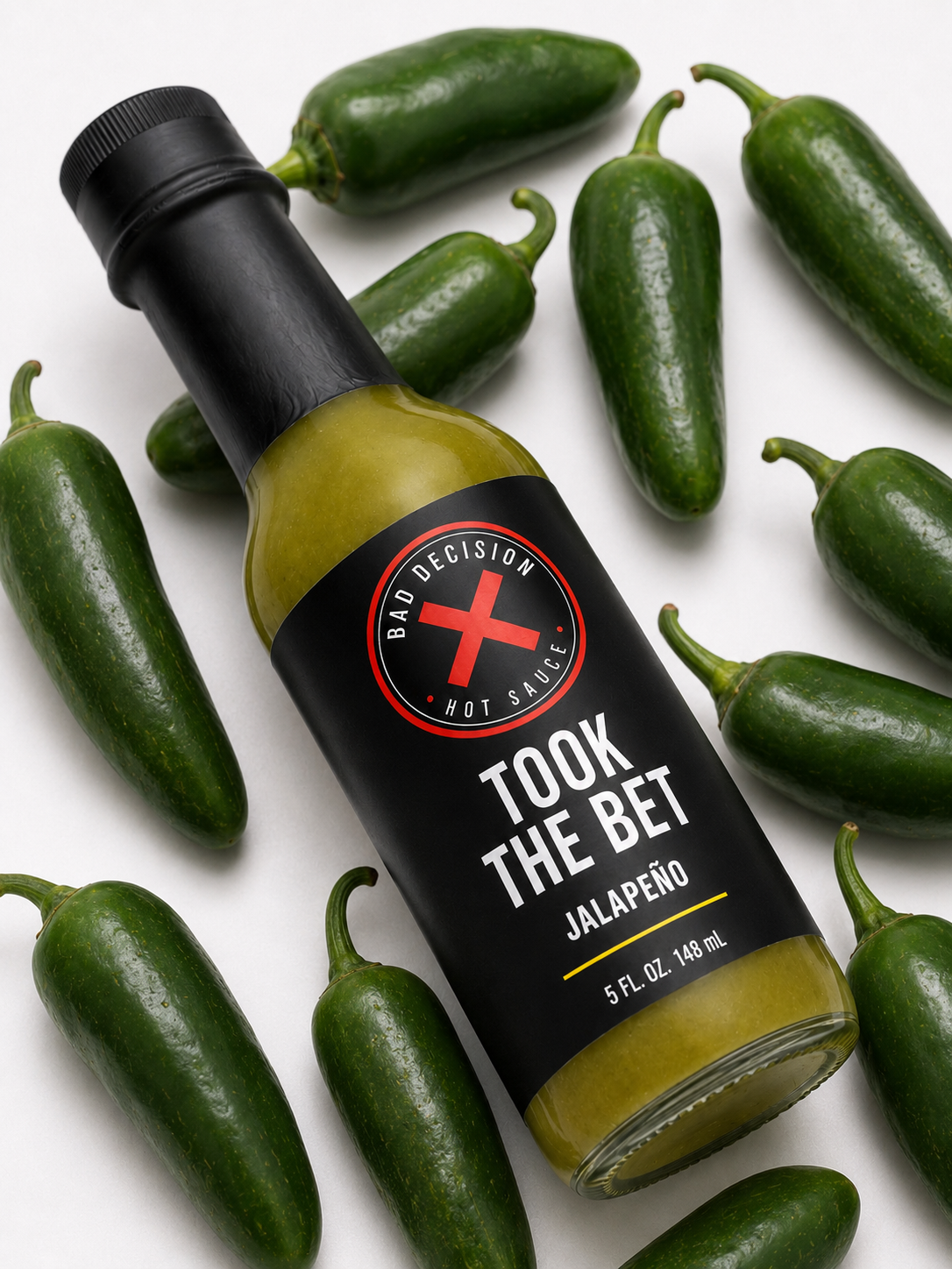 Close-up of Took The Bet jalapeño hot sauce bottle resting among fresh jalapeños