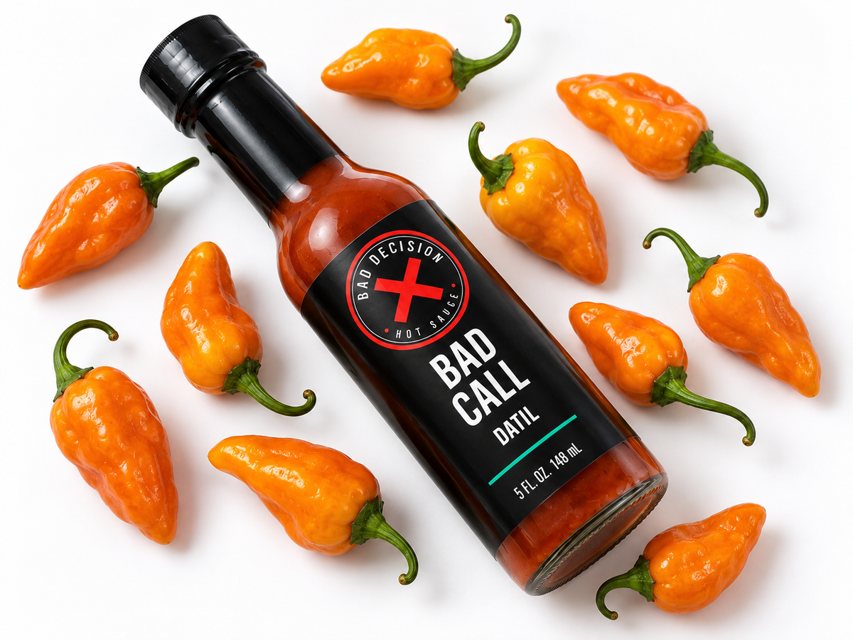 Bad Call datil hot sauce bottle lying among fresh datil peppers