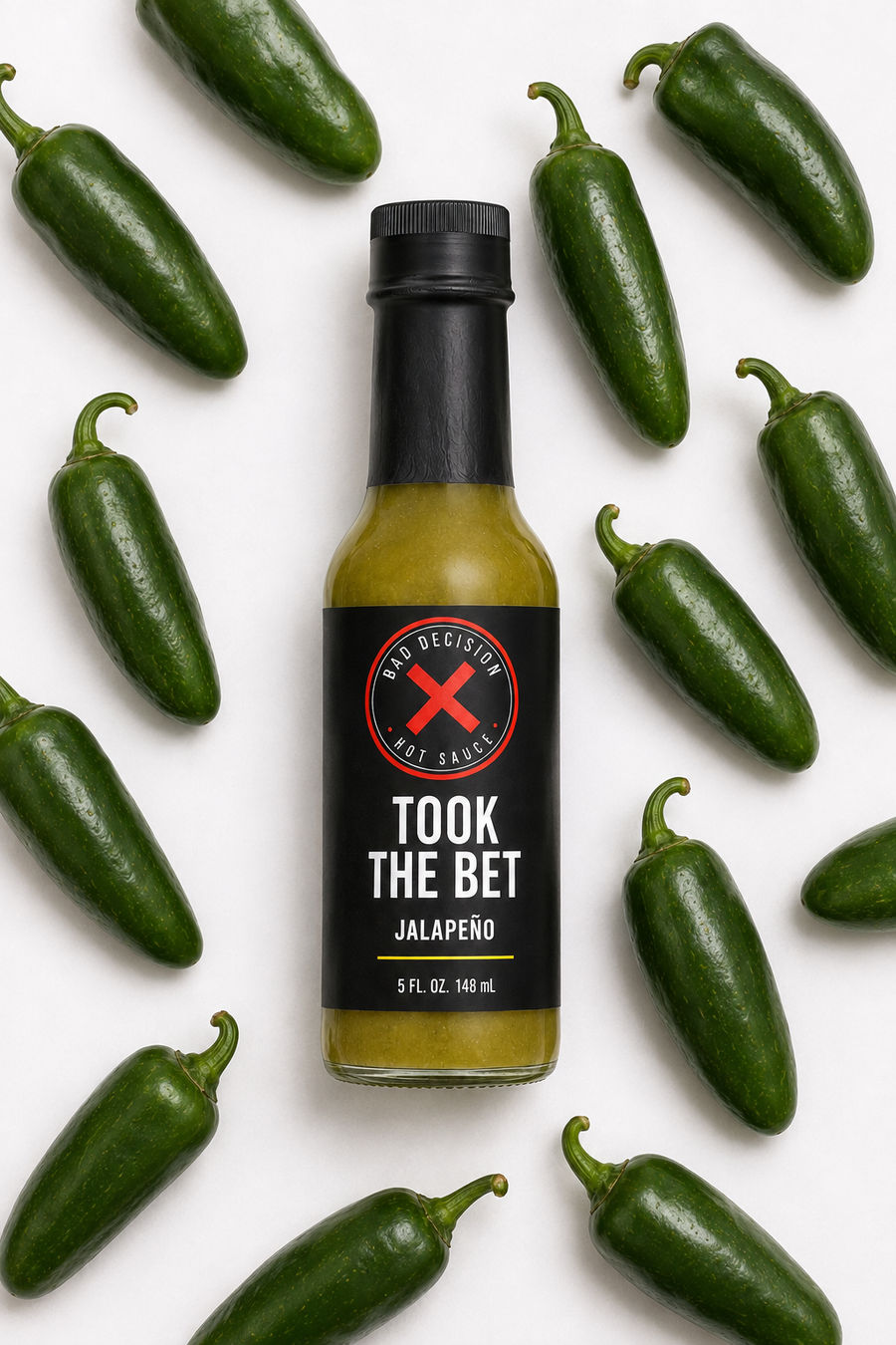 Took The Bet jalapeño hot sauce bottle lying flat among fresh jalapeños on a white background