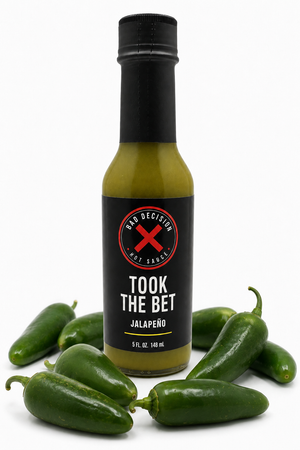 Took The Bet jalapeño hot sauce bottle surrounded by fresh jalapeño peppers