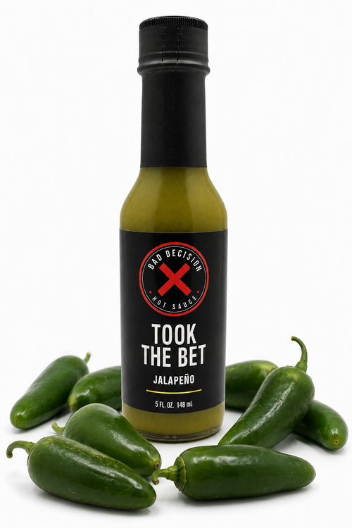 Took The Bet jalapeño hot sauce bottle surrounded by fresh jalapeño peppers