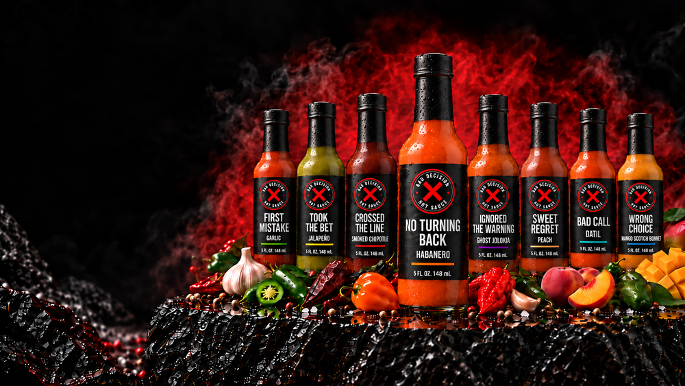 All eight Bad Decision Hot Sauce bottles lined up with fresh garlic, peppers, peach and mango — the full table we bring to market